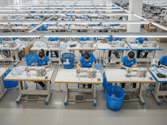 A panoramic view overlooking a modern Chinese garment factory workshop, with neatly arranged sewing machines and cutting equipment. Workers in uni